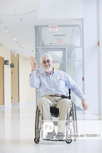 Universitätsprofessor mit Muskeldystrophie winkt mit der Hand in einem Korridor der Universität