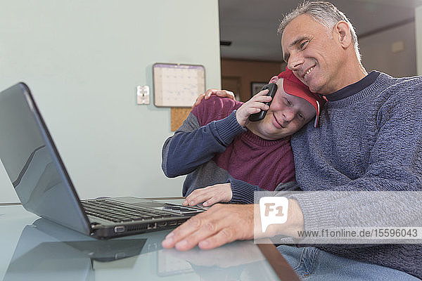 Junger Mann mit Down-Syndrom umarmt seinen Vater mit Rückenmarksverletzung zu Hause