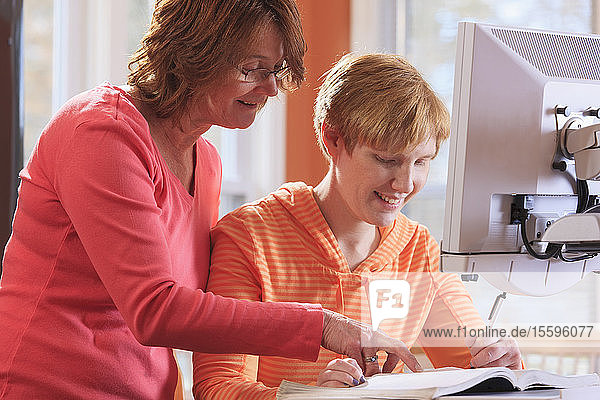 Junge Frau mit Sehbehinderung und ihre Mutter bei der Arbeit an ihrer Schreibtischlupe