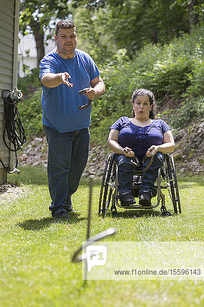 Frau mit Spina Bifida im Rollstuhl spielt Hufeisen mit ihrem Mann
