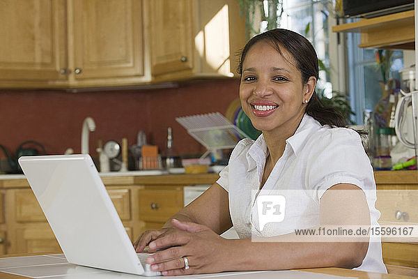 Hispanische Geschäftsfrau  die in der Küche an einem Laptop arbeitet