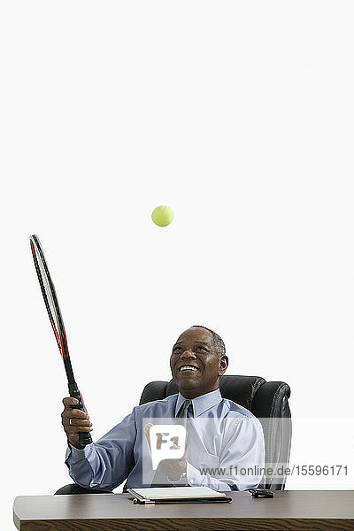 Geschäftsmann sitzt am Schreibtisch und wirft einen Tennisball
