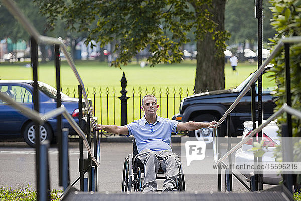 Mann mit Querschnittslähmung im Rollstuhl nähert sich einer Rollstuhlrampe im Freien