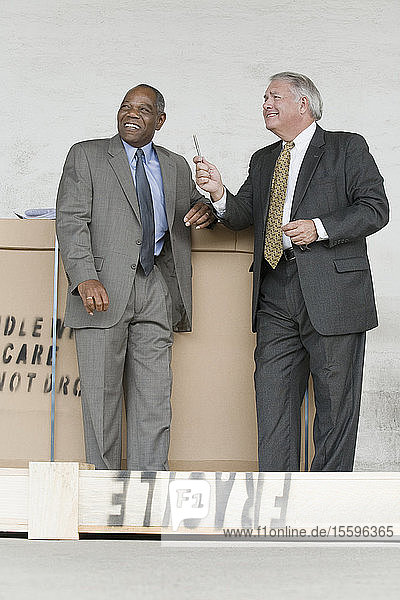 Zwei Geschäftsleute lehnen lächelnd an einer Pappschachtel