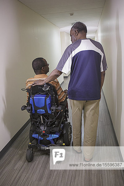 Mann mit Guillain-Barre-Syndrom im Wohnungsflur auf einem elektrischen Rollstuhl mit seinem Vater