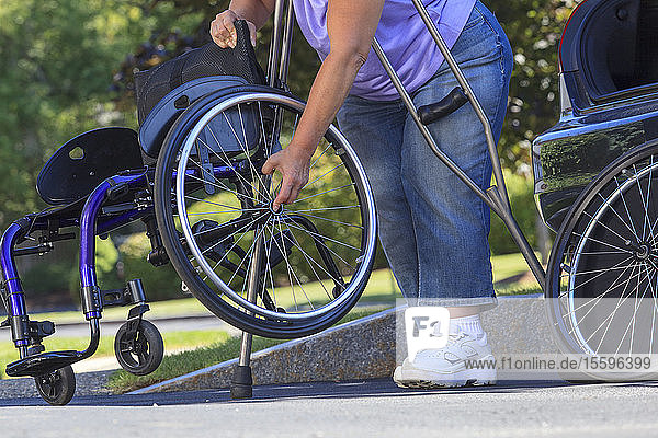 Frau mit Spina Bifida benutzt Krücken  um den Rollstuhl nach einer Reise im Auto zusammenzusetzen
