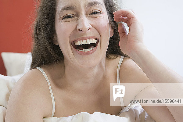 Porträt einer mittleren erwachsenen Frau  die auf dem Bett liegt und lacht