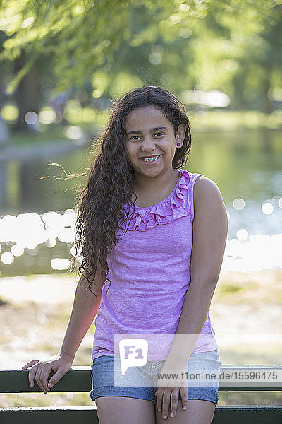 Porträt eines glücklichen hispanischen Teenager-Mädchens mit Zahnspange  das im Park sitzt