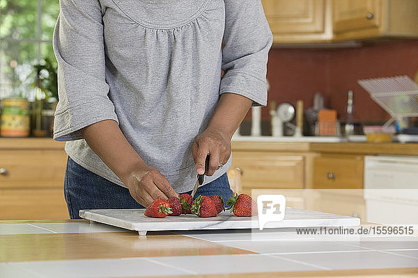 Hispanische Frau schneidet Erdbeeren in der Küche