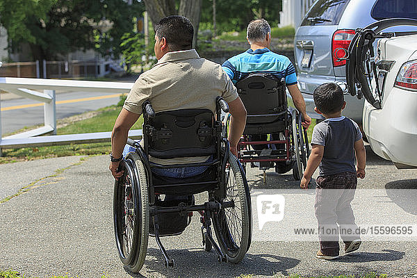 Friends with Spinal Cord Injuries in wheelchairs with a child at car park