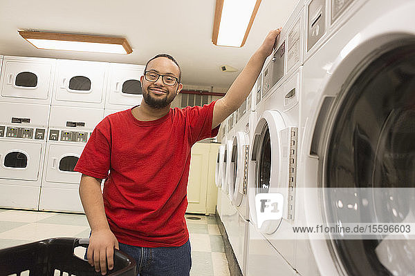 Glücklicher afroamerikanischer Mann mit Down-Syndrom beim Wäschewaschen im Hauswirtschaftsraum