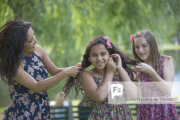 Glückliche hispanische Mutter mit zwei Teenager-Töchtern mit Zahnspange  die sich im Park die Haare machen