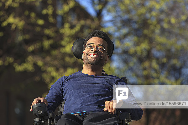Glücklicher afroamerikanischer Mann mit Cerebralparese  der draußen seinen Elektrorollstuhl benutzt