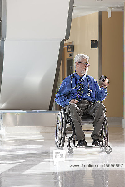 Arzt mit Muskeldystrophie und Diabetes in seinem Rollstuhl  der ein Smartphone benutzt