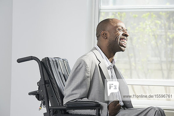 Geschäftsmann mit zerebraler Lähmung sitzt im Rollstuhl und lächelt