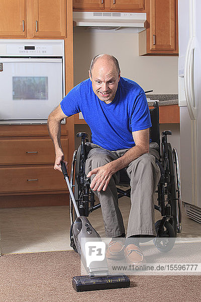 Mann mit Friedreich-Ataxie und deformierten Händen saugt vom Rollstuhl aus sein Haus