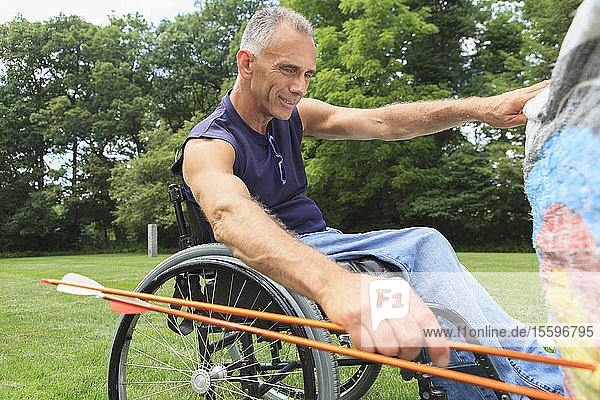 Man with spinal cord injury in wheelchair removing arrows from target after archery practice