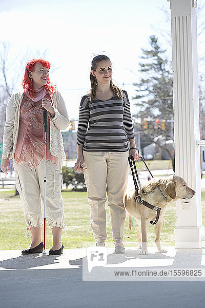 Two women with visual impairments  one with a service dog and one with a cane