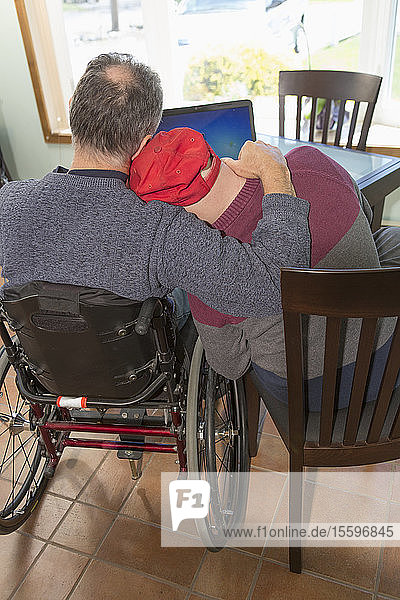 Young man with Down Syndrome hugging his father in wheelchair with Spinal Cord Injury at home
