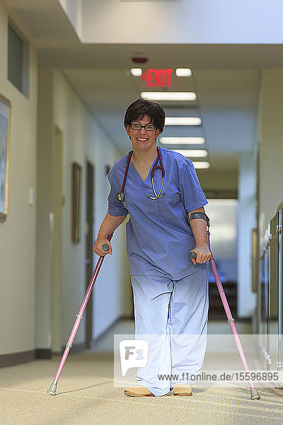 Krankenschwester mit Cerebralparese geht mit ihren Stöcken den Flur einer Klinik entlang