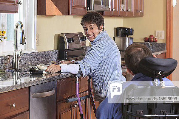 Frau mit Cerebralparese benutzt Krücken und arbeitet in ihrer Küche  während sie mit ihrem Mann mit Cerebralparese spricht