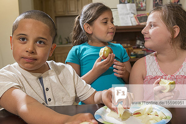Hispanischer Junge mit Autismus isst mit seinen Schwestern zu Hause einen Apfel