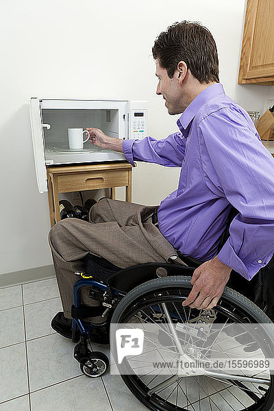 Mann im Rollstuhl mit Rückenmarksverletzung entnimmt Tasse aus einer zugänglichen Mikrowelle