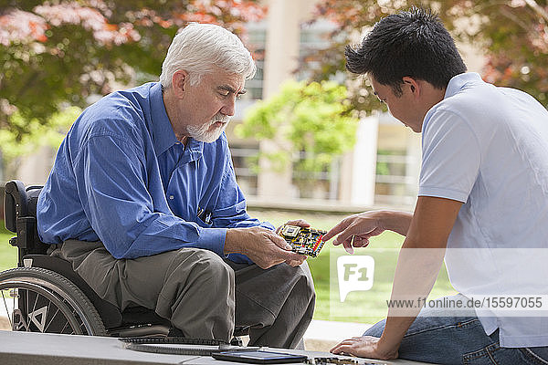 Engineer with muscular dystrophy and diabetes in his wheelchair talking with design engineer about microchips on circuit board