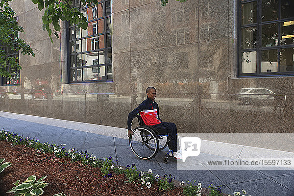 Man in wheelchair who had Spinal Meningitis using a city sidewalk
