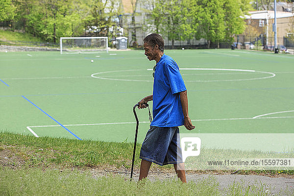Mann mit traumatischer Hirnverletzung beim Spaziergang mit seinem Stock in der Nähe einer Schule