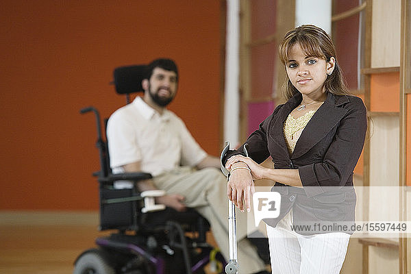 Porträt einer behinderten Frau mit einem im Rollstuhl sitzenden Mann im Hintergrund.