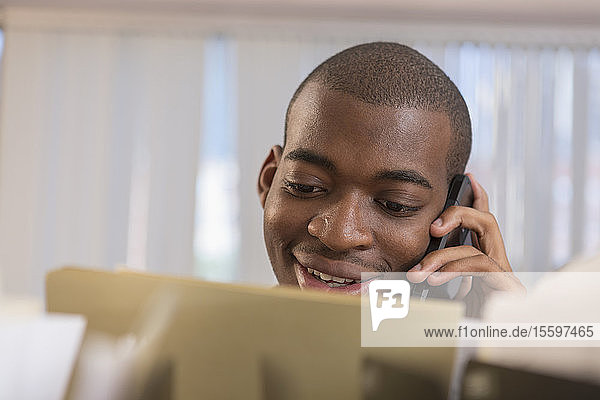 Happy African American man with Autism talking on cell phone while working in an office