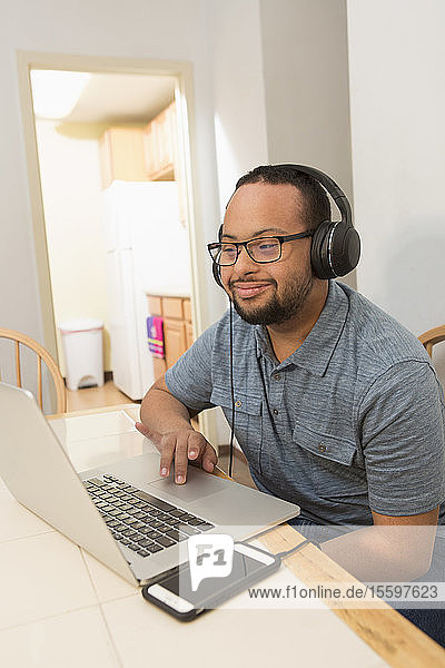 Glücklicher afroamerikanischer Mann mit Down-Syndrom  der zu Hause einen Laptop benutzt und Musik hört