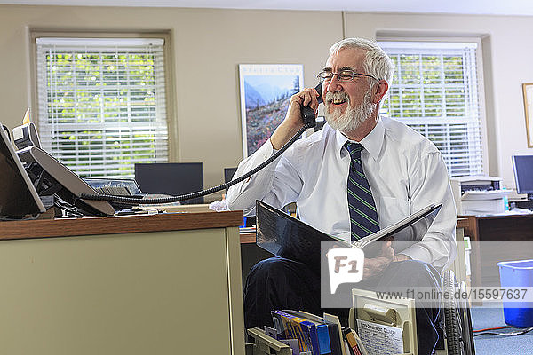Mann mit Muskeldystrophie im Rollstuhl am Telefon in seinem Büro