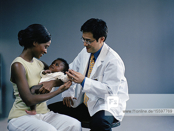 Junge Frau  die ihr kleines Baby hält  während ihr männlicher Arzt dabei ist