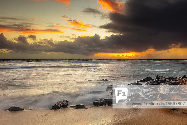 Sonnenaufgang über Strand und Meer mit einer Sturmwolke und Regen in der Ferne; Kauai  Hawaii  Vereinigte Staaten von Amerika