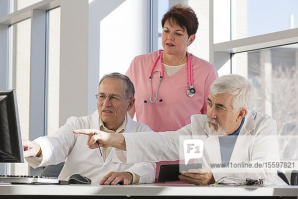 Zwei Ärzte und eine Krankenschwester diskutieren an einem Computer und einem Tablet. Ein Arzt hat Muskeldystrophie