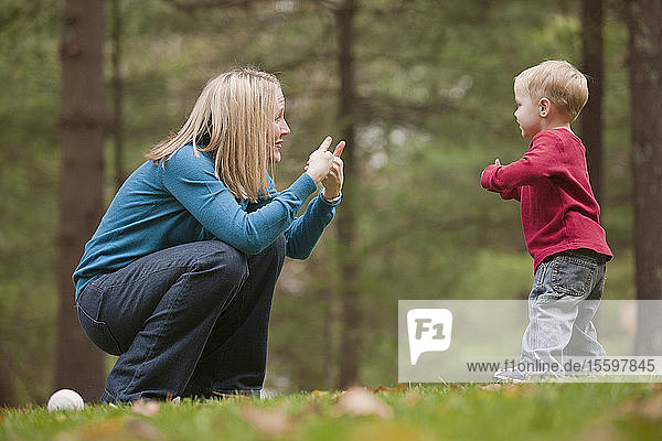 Woman signing the word 'Game' in American Sign Language while communicating with her son in a park