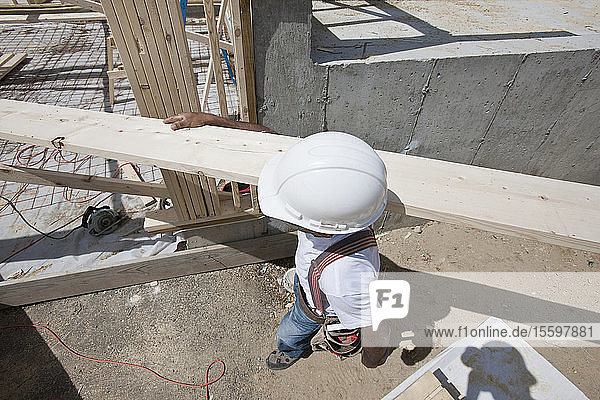 Zimmermann trägt eine Planke auf einer Baustelle