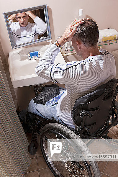 Mann mit Rückenmarksverletzung im Rollstuhl beim Frisieren seiner Haare