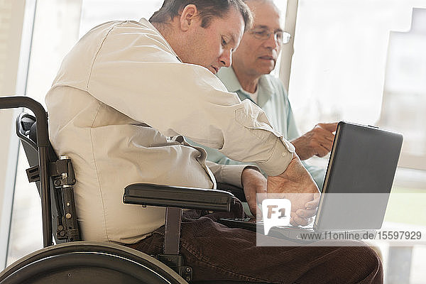 Quadriplegic man with spinal cord injury in wheelchair using his thumb to type on computer