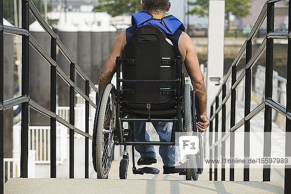Rückansicht eines Mannes  der in einem Rollstuhl auf einer Rollstuhlrampe sitzt