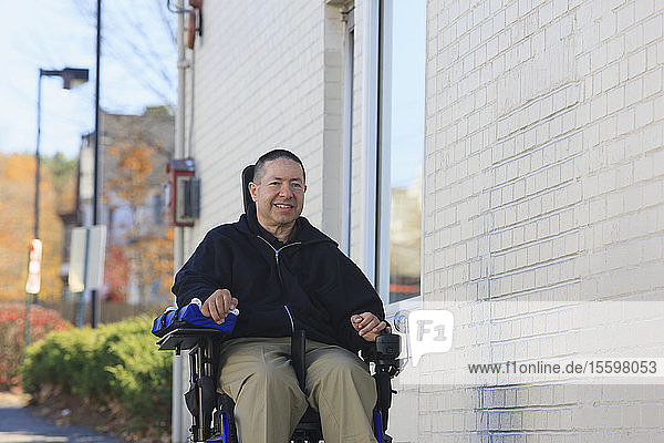 Mann mit Rückenmarksverletzung und Arm mit Nervenschaden im motorisierten Rollstuhl auf einer öffentlichen Straße