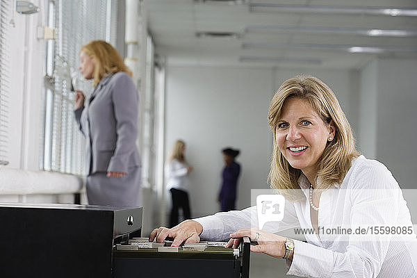 Porträt einer fröhlichen Geschäftsfrau  die einen Aktenschrank öffnet.