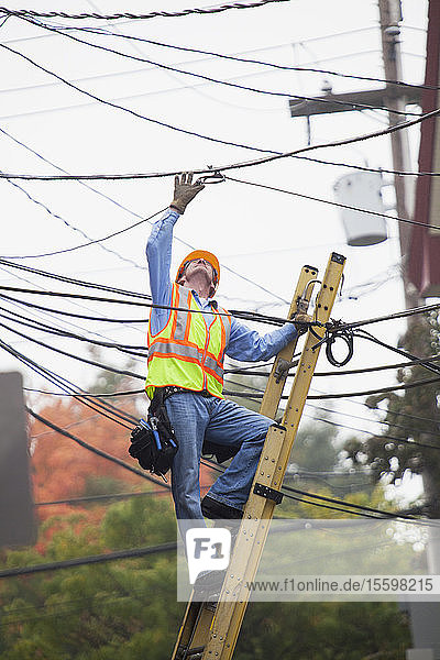 Kabelmonteur  der von einer Leiter aus eine Kabelverbindung in der Stadt überprüft