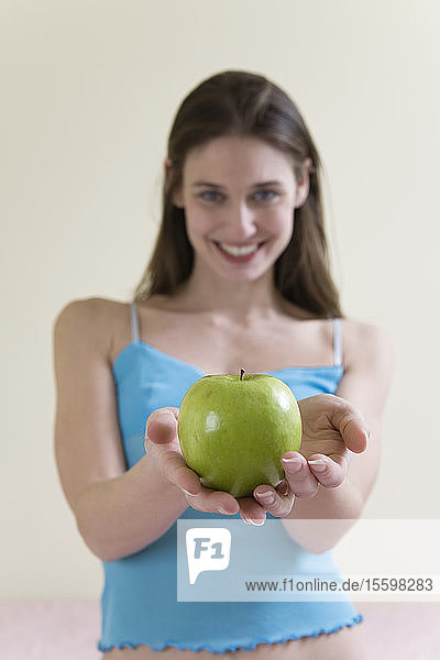 Eine schöne junge Frau hält einen grünen Apfel.