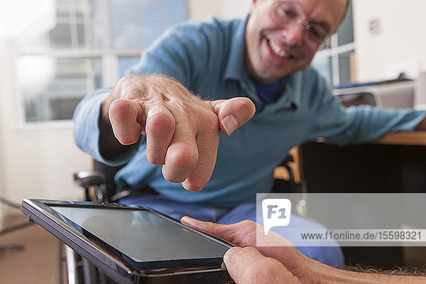Two disabled men sitting in wheelchairs and using a digital tablet  one with deformed hands