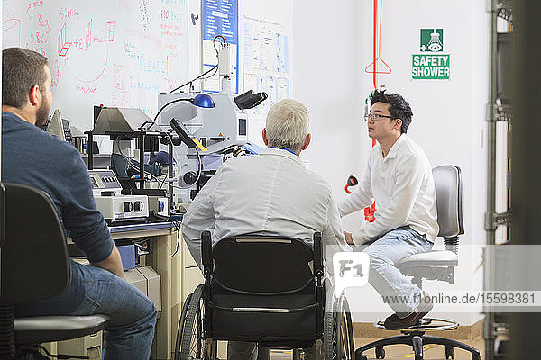 Professor mit Muskeldystrophie und Ingenieurstudenten bei der Überprüfung von Verfahren für ein Röntgenfluoreszenzexperiment in einem Labor