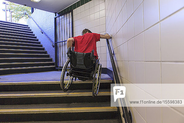 Trendy man with a spinal cord injury in wheelchair going down subway stairs backwards