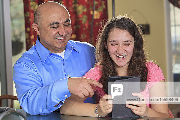 Father and daughter laughing at a tablet message
